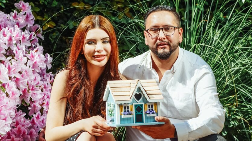 A friendly man and and a woman holding a dollhouse and looking at camera